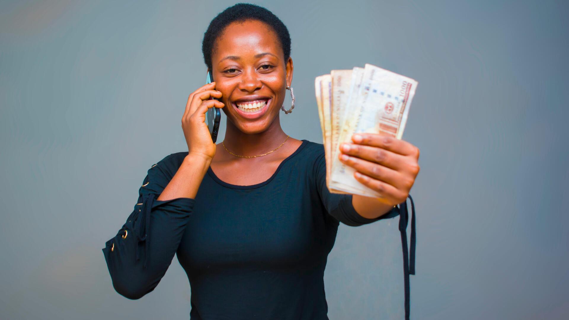 Femme souriante au téléphone tenant des billets après une vente